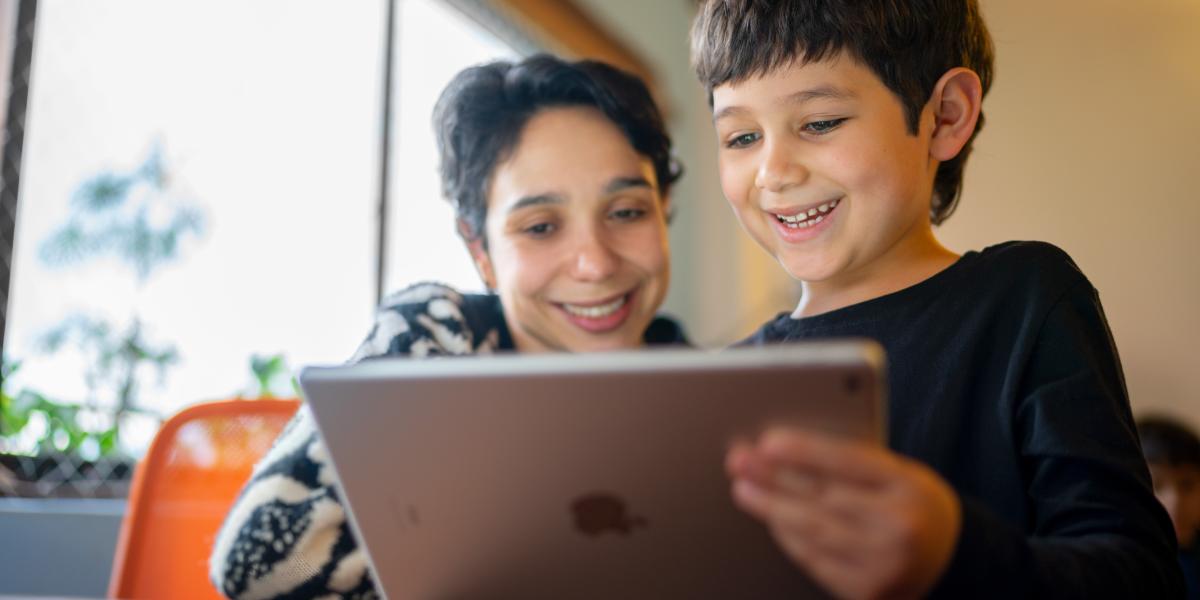 Eine Mutter und ihr Sohn im Volksschulalter bedienen in einer Wohnumgebung gemeinsam ein iPad