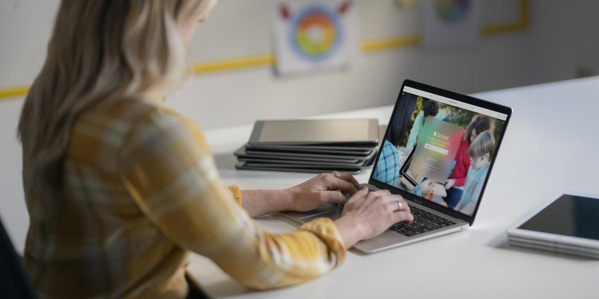 Eine IT-Administratorin verwaltet auf einem MacBook die Geräte ihrer Schule, im Hintergrund ein Stapel iPads