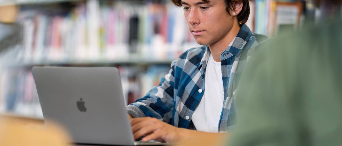 Ein Student sitzt in einer Bibliothek vor einem MacBook Air