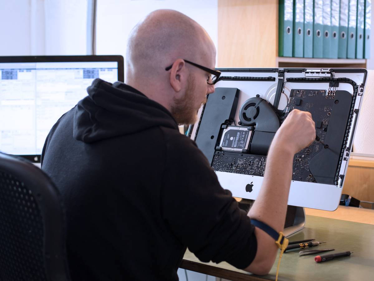 Nico Sieder, Tools at Work Spezialist im Apple Service, repariert einen iMac, der mit geöffnetem Gehäuse auf seinem Arbeitstisch steht