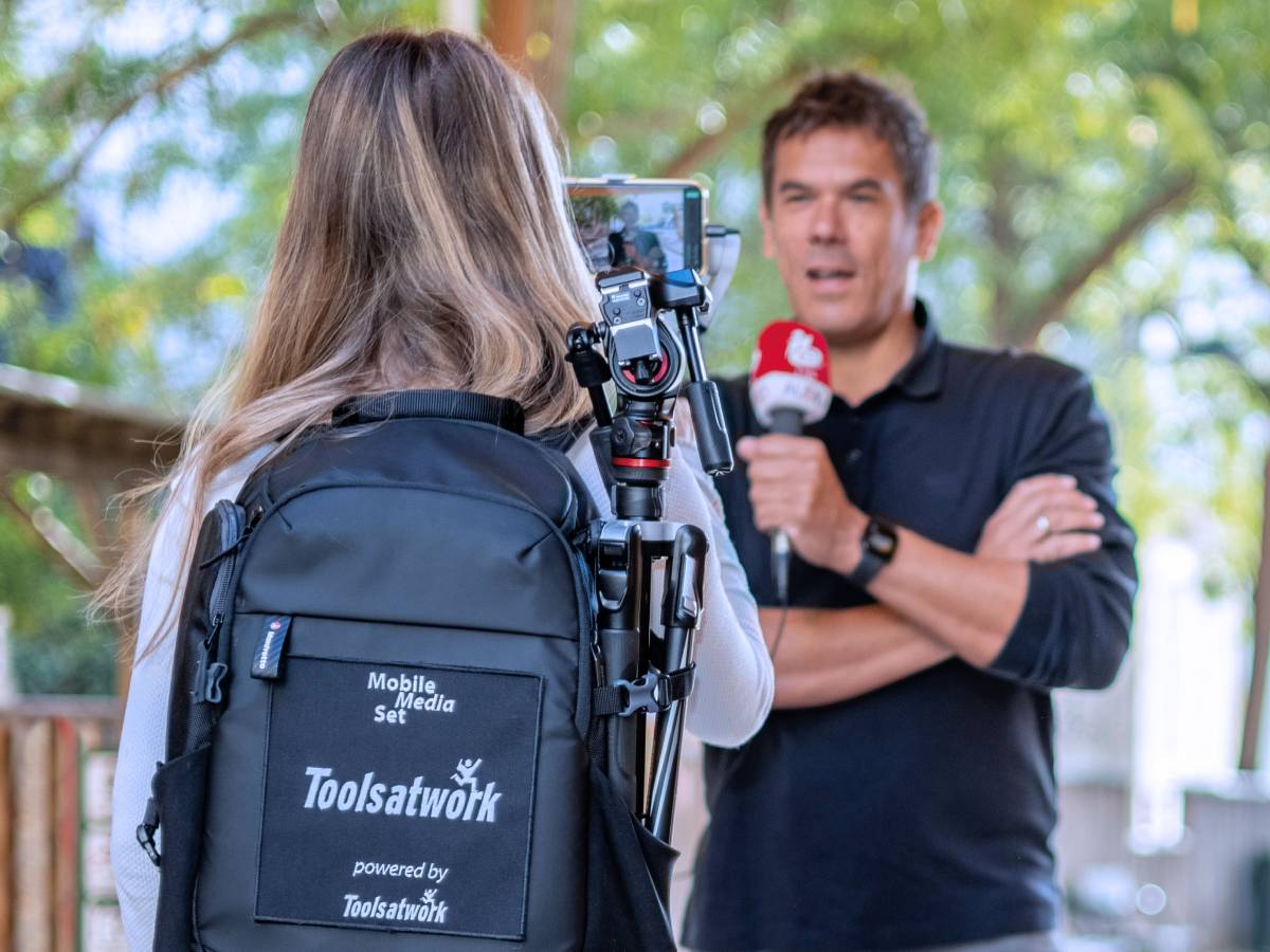 Oliver Deutsch, Tools at Work Bereichsleiter Video/Audio spricht in ein Handmikrofon, im Vordergrund Claudia Söllner, Tools at Work Spezialistin Apple Verkauf, mit dem MobileMediaSet Rucksack