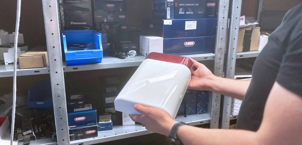 Ein Mitglied des Tools at Work Sicherheitstechnik Teams hält die Außensirene einer Alarmanlage in Händen